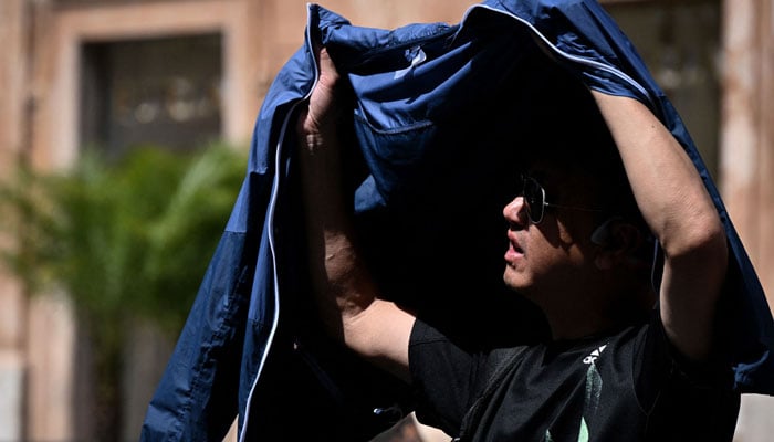 A man uses a jacket to shield himself from the sun in front of the Scalinata di Trinita dei Monti (Spanish Steps) in Rome on July 18, 2023. — AFP