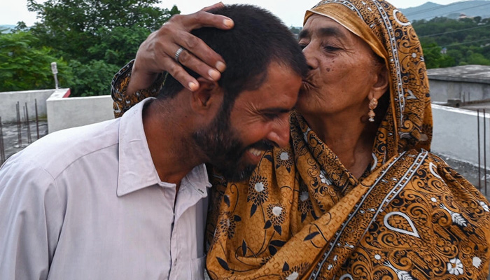 In this picture taken on July 18, 2023, Muhammad Naeem Butt, who gave up on a perilous attempt to reach Europe, is kissed by his mother Razia Latif at their home in Pakistan. — AFP