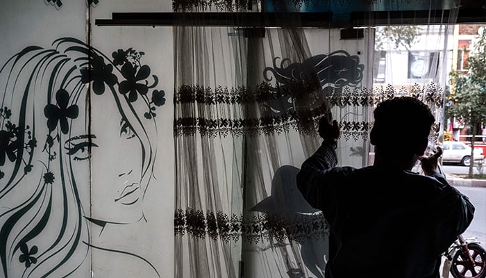 An afghan man remove curtains inside a beauty parlour in Kabul on July 25, 2023. — AFP