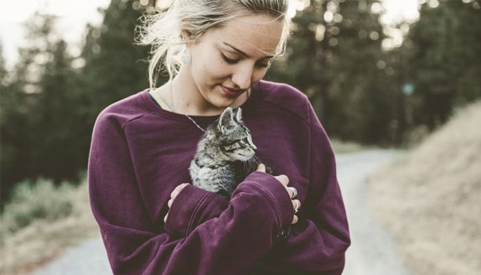 A pet parent snuggles her cat while taking a walk outside. — Unsplash/File