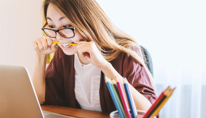 A concerned student bites a pencil while looking at a laptop. — Unsplash/File