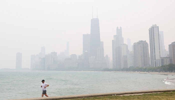 A jogger runs along the shoreline of Lake Michigan with heavy smoke from the Canadian wildfires in the background, on June 27, 2023, in Chicago, Illinois. — AFP