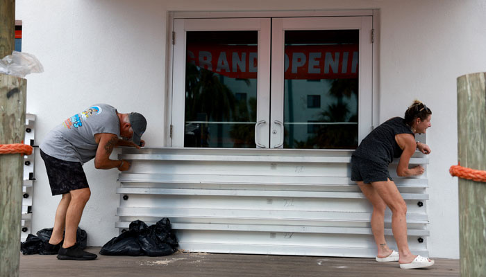 (L-R) Steve Leitgeb and Michelle Fedeles place protective shutters over the openings at Coco´s Crush Bar & Grill before the possible arrival of Hurricane Idalia on August 29, 2023 in Indian Rocks Beach, Florida. AFP