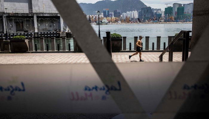 A man runs past glass with tape on it in Hong Kong on August 31, 2023, a day before the arrival of Typhoon Saola. — AFP