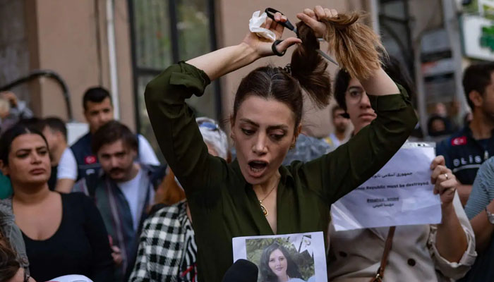 A woman protester cutting her hair in Jina Mahsa Amini protests outside Iran. — AFP