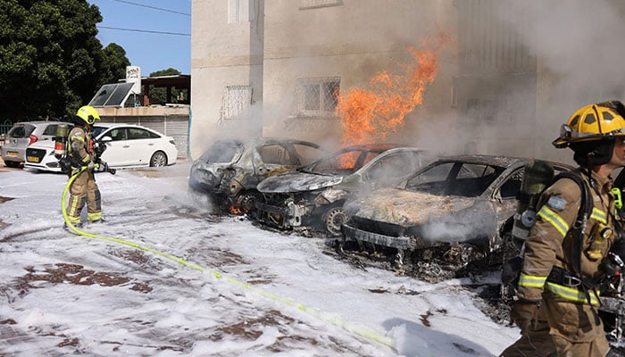 A member of Israeli security forces tries to extenguish fire on cars following a rocket attack from the Gaza Strip in Ashkelon, southern Israel, on October 7, 2023. — AFP