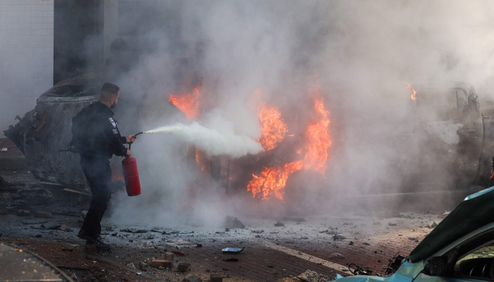 A member of Israeli security forces tries to extinguish fire on cars following a rocket attack from the Gaza Strip in Ashkelon, southern Israel, on October 7, 2023. — AFP