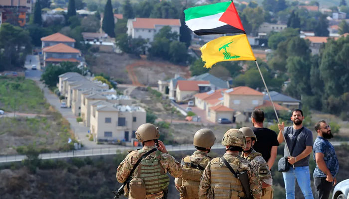 Lebanese soldiers stand on a hill overlooking the Israeli town of Metula as a man waves the Palestinian and Hezbollah flags at the Lebanese-Israeli border in the southern village of Kafr Kila, Lebanon, on October 9, 2023. —AFP