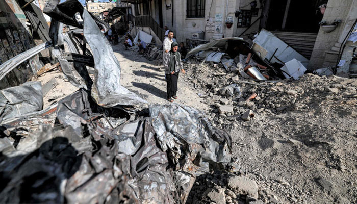 People stand by rubble and the remains of a destroyed vehicle outside a mosque in the occupied West Bank city of Jenin on July 5, 2023. — AFP