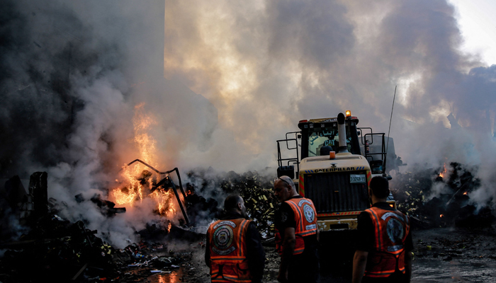 Smoke and fire rise from buildings as rescuers gather amid the destruction in the aftermath of an Israeli strike on Gaza City on October 26, 2023. — AFP