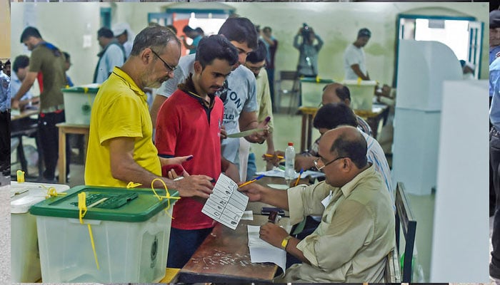 25 Temmuz 2018'de Lahor'daki bir sandık merkezinde Pakistan genel seçimlerinde oy verme sırasında seçim yetkilileri oy pusulalarını kontrol ederken Pakistanlı erkekler sıraya giriyor. — AFP