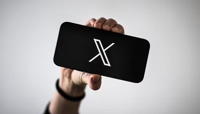 A woman holds a smartphone displaying the logo of social network X (formerly Twitter). — AFP