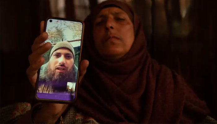 The mother of Azad Yousuf Kumar holds a smartphone displaying her sons photos, wearing a military uniform, at the Pulwama village in India. — Business Insider via SOPA