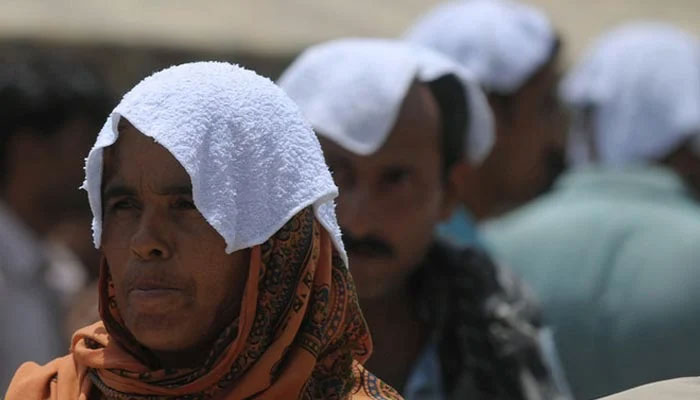 People stand under the sun with their heads covered with wet towels during a heatwave in Karachi on June 29, 2015. — AFP/File