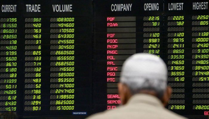 پاکستانی تاجر پاکستانی اسٹاک ایکسچینج (PSX) میں حصص کی قیمتیں دکھانے والے الیکٹرانک بورڈ کے نیچے کھڑے ہیں۔  - INP/فائل