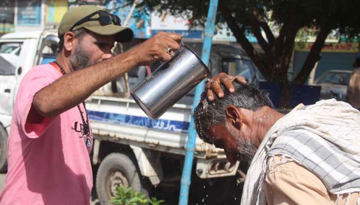 volunteer showers water on a labourers head to protect him from heat stroke during high temperatures in Karachi. — Online/File