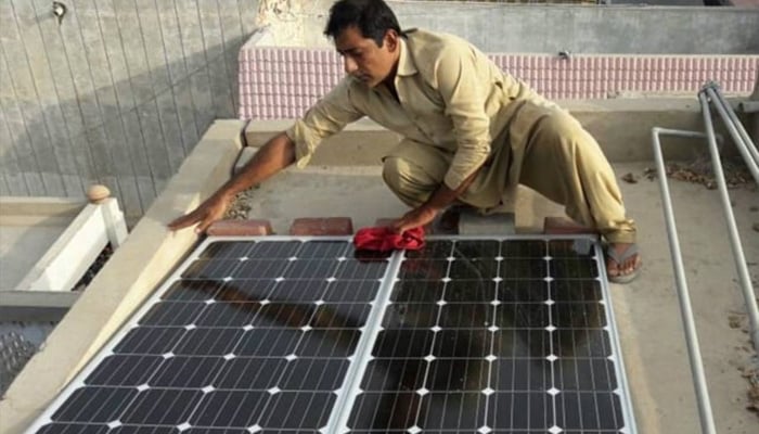 A man wipes the dust off solar panels he recently installed on the roof of his home in Larkana, in Pakistan’s Sindh province, June 28, 2017. — Reuters