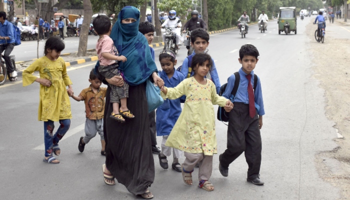 A woman is carrying her children while crossing a busy road after school time in Lahore on May 3, 2024. —Online