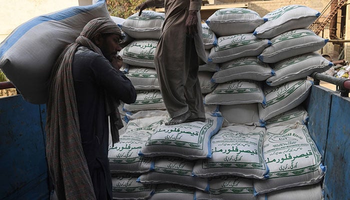 Labourers load sacks of wheat flour at a market in Karachi. — AFP/File