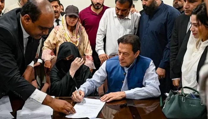 Former prime minister Imran Khan (right) along with his wife Bushra Bibi (centre) signs surety bonds for bail in various cases, at the registrars office in the Lahore High Court on July 17, 2023. — AFP