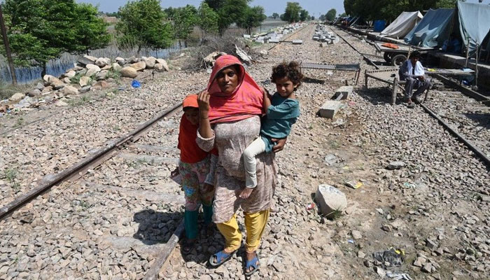 Fahmidah, a pregnant flood-affected woman carries her child as she walks near her tent at a makeshift camp along a railway track in Fazilpur, Rajanpur district of Punjab province on September 3, 2022. — AFP