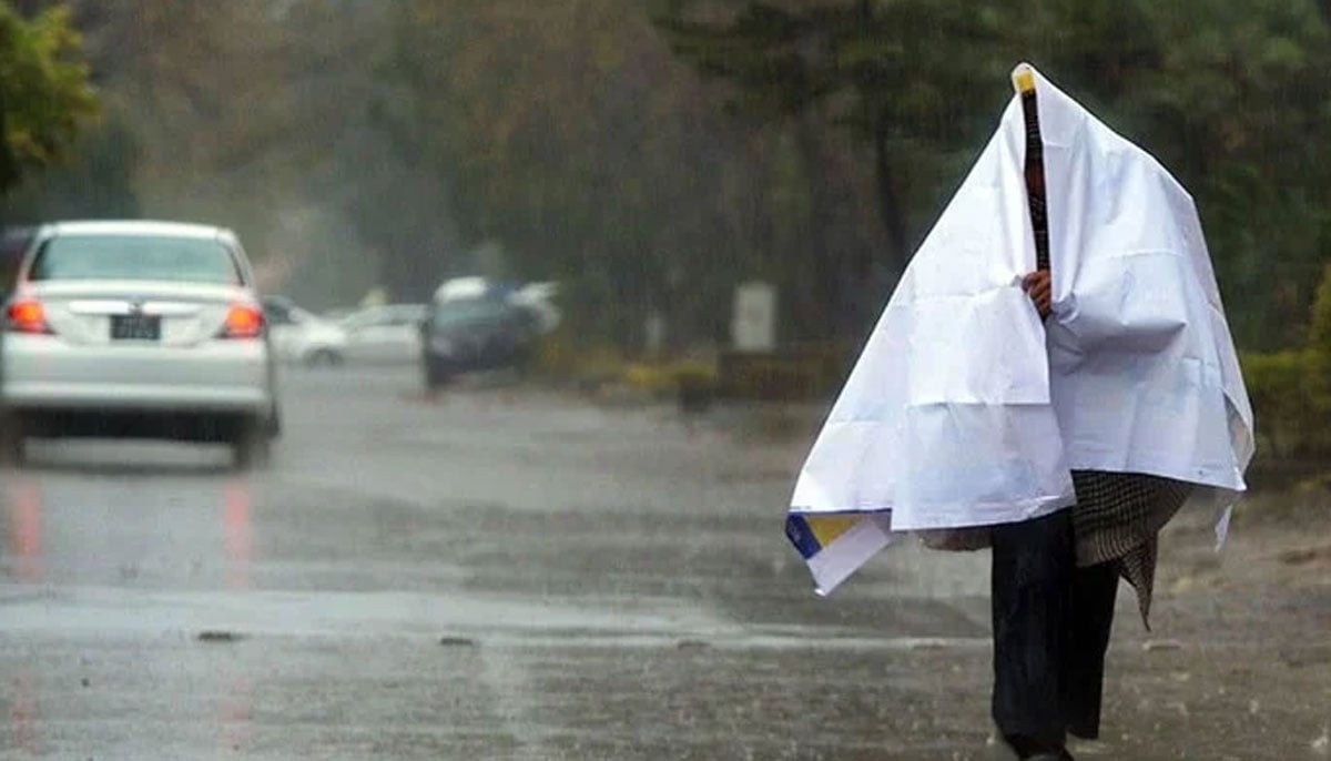 A man walks on a road while covering himself with a sheet during a rainy day. — AFP/File