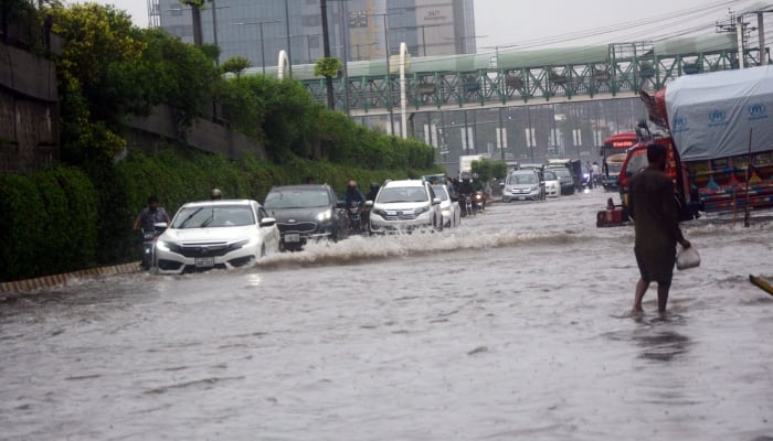 Vehicles crossing road flooded with rainwater after heavy rain in Lahore on July 22, 2023. —APP