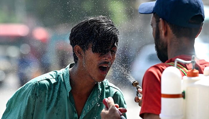 A volunteer sprays water on a bypasser’s face along a street during a hot summer day in Karachi, May 30, 2024, amid the ongoing heatwave. — AFP