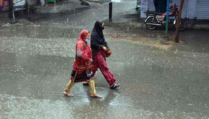 Women passing through a road during heavy rain on March 24, 2023. — Online