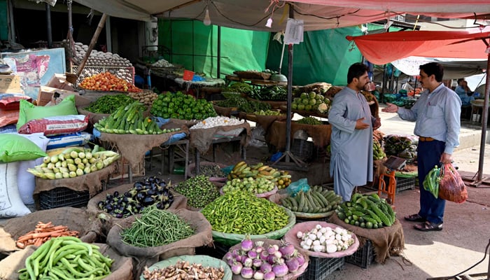 ایک سبزی فروش (L) 3 جون 2024 کو اسلام آباد کی ایک مارکیٹ میں ایک گاہک سے ملاقات کر رہا ہے۔ - AFP