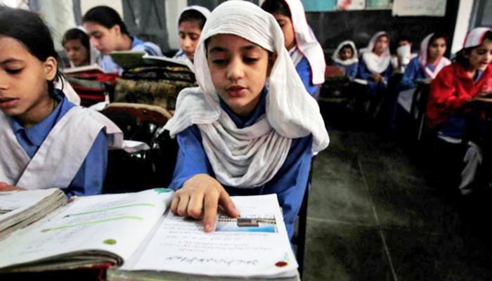 A girl reading a book while attending her daily class with others at a government school in Peshawar. — Reuters/File