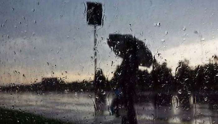 Rain water falls on a glass window as a passer by walks on a street in Karachi. — AFP/File