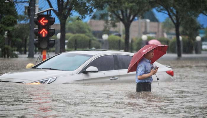 A man wades past a submerged car along a flooded street following heavy rains in Zhengzhou, China, July 20, 2021. — AFP