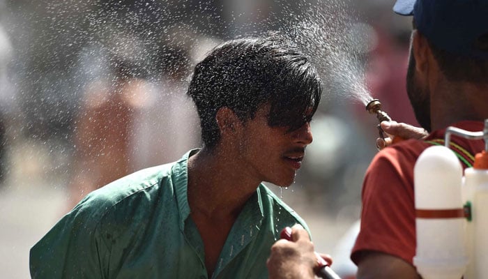 A Edhi volunteer sprays water on a bypassers face along a street during a hot summer day in Karachi on May 30, 2024. — INP