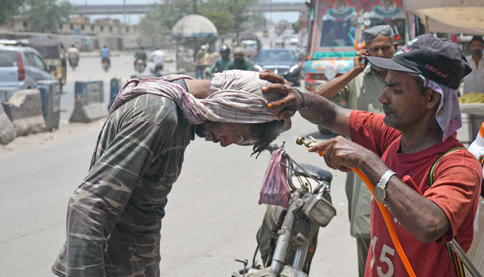 Volunteer sprays water on commuters to cool off during a hot summer day along a street in Karachi on June 26, 2024. — Online