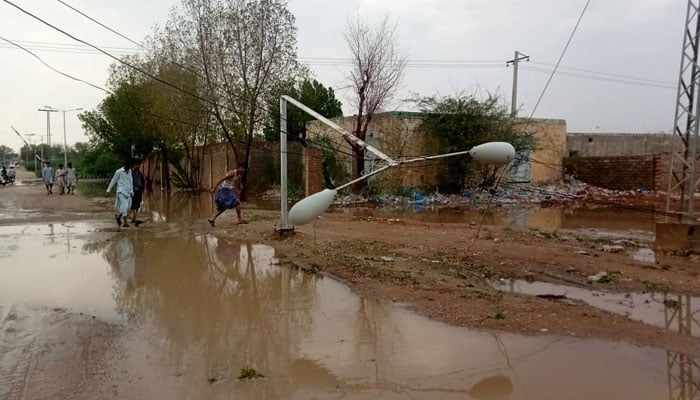 Residents can be seen walking past by a knocked down street light pole due to heavy rains in Balochistan. — Reporter