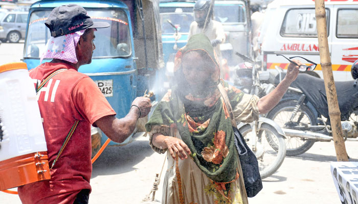 A volunteer sprays water on passengers to cool them down during a hot summer day on a street in Karachi on June 26, 2024. — Online