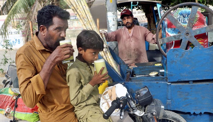 Father and son beat the heat with traditional sugarcane juice while sitting on their bike in Karachi. — APP/File