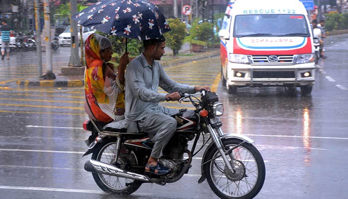 Representational image of a woman holds an umbrella to shield her famil from the rain while riding a motorcycle in the Lahore on July 6, 2024. — AFP