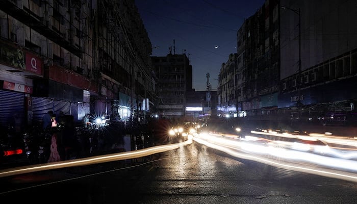 Vehicle lights cause light streaks on the road along a market in Karachi on January 23, 2023. — Reuters