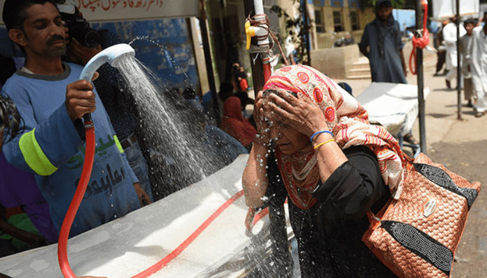 A volunteer showers a woman with water during a heatwave in Karachi. — AFP/File