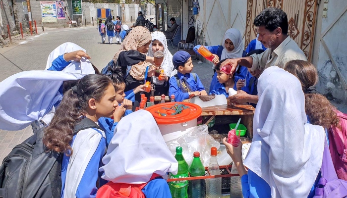 Schoolchildren busy in purchasing ice balls from street vendor during hot day at the Committee Chowk in Rawalpindi on May 20, 2024. —APP