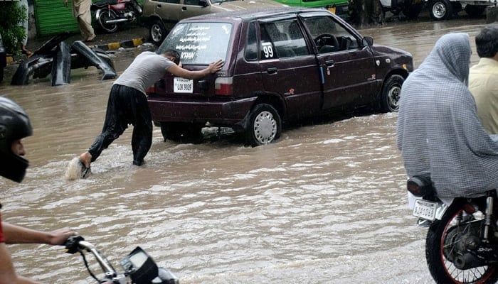 an pushes a car breaks down due to submerged rainwater in Lahore. — NNI/File