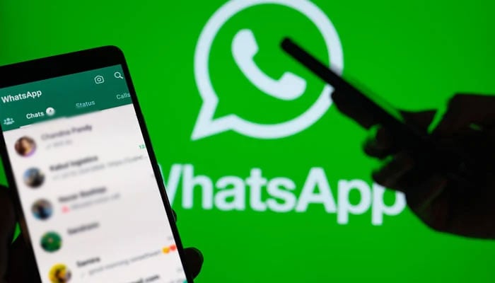 WhatsApp logo seen in the background with a person using the application on his phone. — CNBC/File