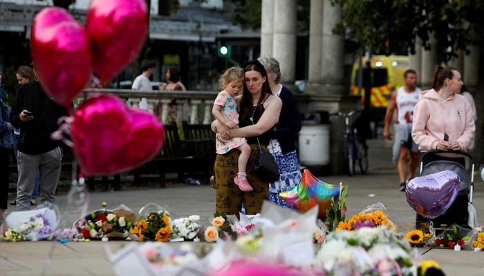 A woman holding her child, looks at the floral tributes following a vigil for the victims of a knife attack in Southport, Britain July 30, 2024. — Reuters