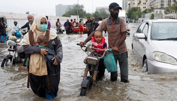 A family wades through a flooded road during the monsoon season in Karachi, July 9, 2022. — Reuters