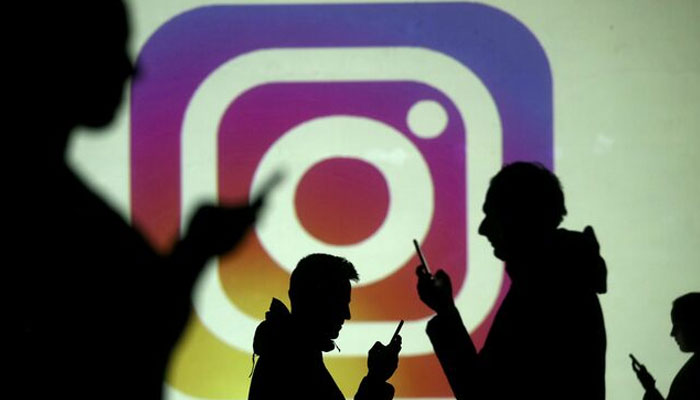 Silhouettes of mobile users are seen next to a screen projection of the Instagram logo in this picture illustration taken March 28, 2018. — Reuters