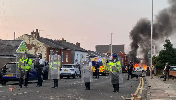 Protesters set a fire as riot police stand guard near the Southport Islamic Society Mosque. — AFP/File