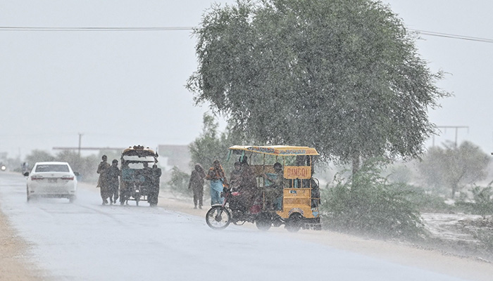 Commuters make their way along a street during rainfall on the outskirts Dadu on August 4, 2024. — AFP