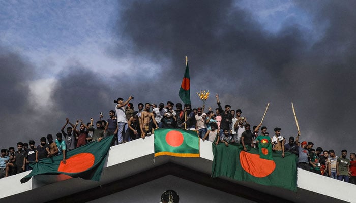 Demonstran antipemerintah mengibarkan bendera nasional Bangladesh saat menyerbu istana Perdana Menteri Sheikh Hasina di Dhaka pada 5 Agustus 2024. — AFP